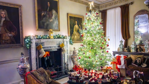 The Music Room at Erddig Hall, Wrexham, with an ornately decorated Christmas tree with baubles and fairy lights, surrounded by gifts. Stockings hand on the fireplace and Father Christmas' coat hangs over a chair.